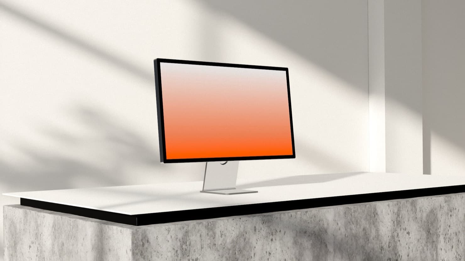 A Studio Display on a white desk over a concrete plinth, lit by soft daylight through a window.